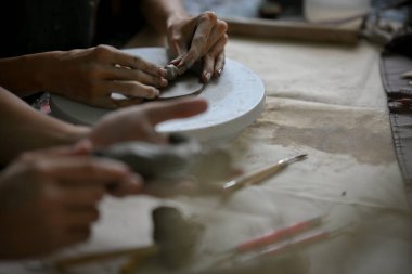 Küçük bir çömlek çarkına işlenmemiş kil şekillendiren ya da şekillendiren bir erkeğin yakın plan resmi, sanat atölyesinde el yapımı kil süsü yapıyor..