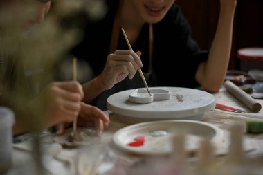 Bir adamın, arkadaşıyla birlikte yaratıcı bir el işi atölyesinde seramik tabak boyamaktan hoşlanan yakın plan görüntüsü. El işi atölyesi konsepti