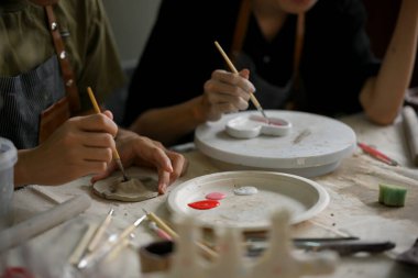 Bir adamın yakın plan görüntüsü, arkadaşıyla birlikte yaratıcı bir el sanatları atölyesinde akrilik renklerle seramik bir tabak boyamaktan zevk alır..