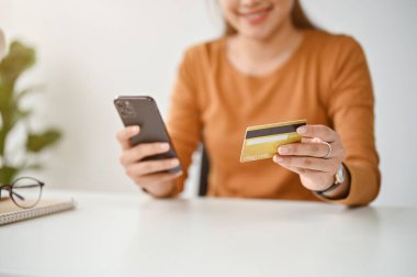Bir kadının yakın plan görüntüsü kredi kartını akıllı telefonuyla alışveriş uygulamasına bağlıyor, evden online alışveriş yapmaktan hoşlanıyor..