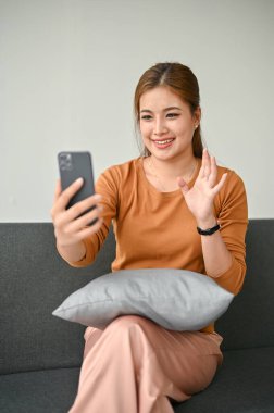 Sıradan kıyafetlerle güzel bir Asyalı kadının portresi. Oturma odasındaki akıllı telefonuyla arkadaşlarıyla sohbet ediyor..