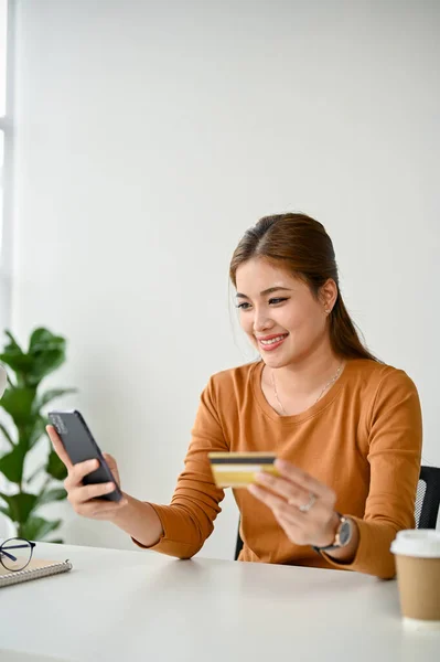 一位迷人的亚洲女人通过她的智能手机将她的信用卡和一个购物应用程序连接起来 她喜欢在家里上网购物 移动银行 信用卡支付 电子商务 — 图库照片