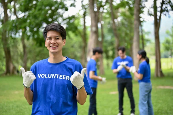 一位快乐的年轻亚洲男性志愿者站在公园里 竖起大拇指 和他的朋友们一起参加清理公园的志愿工作 志愿工作 慈善活动 — 图库照片