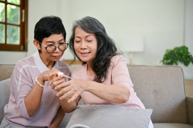 İki mutlu orta yaşlı Asyalı bayan arkadaş oturma odasında yeni makyaj ürünleri deniyorlar. Güzellik ve yaşam tarzı kavramları