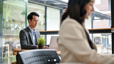 Yakışıklı ve zeki bir Asyalı işadamı ya da resmi takım elbiseli bir ofis çalışanı, bir kafede birlikte çalışırken dizüstü bilgisayarına odaklanır..