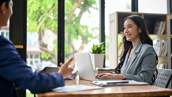 stock image A beautiful millennial Asian businesswoman is listening to her male colleague explain and share his ideas on a new project while working in the office together.