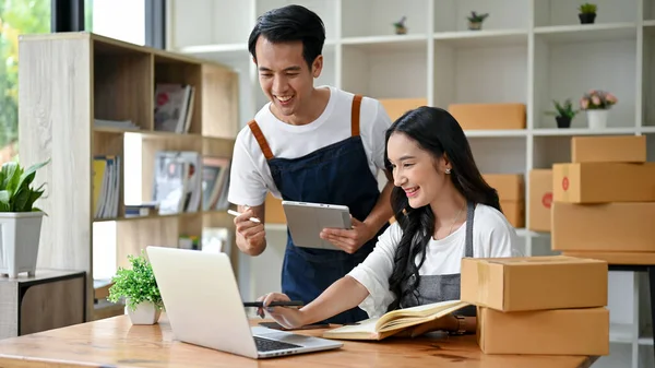 A cheerful and lovely Asian online seller couple is looking down at a laptop screen, excited and happy with their online orders from customers during the big sales season.