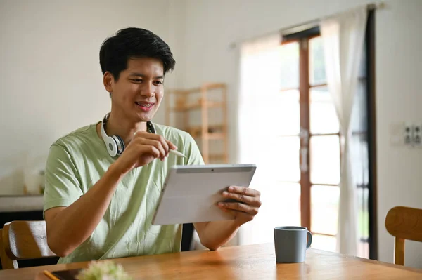 一位身穿休闲装的英俊的亚洲年轻人在客厅的桌上用他的数码平板电脑 — 图库照片