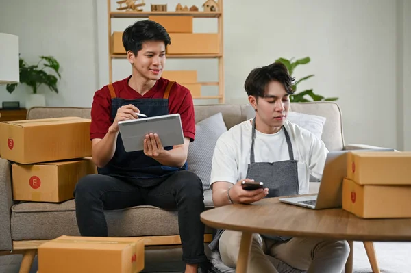 A handsome young Asian male online shop owner checking online orders and updating new products on the shopping website and working with his boyfriend at home. LGBT couple and job concept