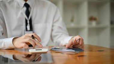 Profesyonel bir Asyalı bankacının hesap makinesi kullanırken ve ofisindeki masasında dolar sayarken yakın plan görüntüsü. mali yatırım, tasarruflar, döviz kuru