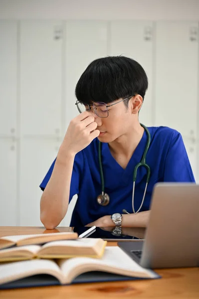 一位穿着洗澡服 压力很大 疲惫不堪的年轻亚裔医科学生正在他房间的一张桌子上做他的医学研究 — 图库照片