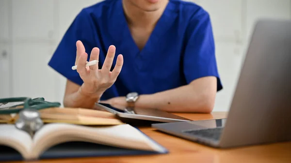 Close-up hand image of a focused male medical student or doctor in scrubs is having an online medical checkup with a patient or joining a medical webinar.