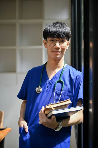 医院走廊里 站着一个身穿洗涤剂和眼镜的积极 专业的年轻亚洲男医生的画像 上面放着书 医务工作者概念 — 图库照片
