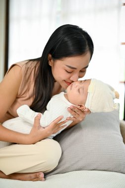 Genç, güzel bir Asyalı anne yatakta otururken bebeğini kollarında tutuyor. Anne ve çocuk kavramı. 