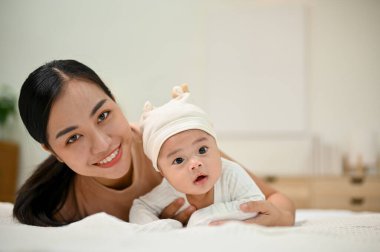 Güzel bir aile anı. Genç Asyalı anne bebeğiyle uzanıp kameraya gülümsüyor. Bebeğine şefkat gösteriyor..