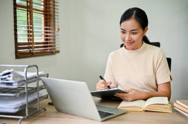 Masasında dijital tabletle çalışan güzel Asyalı kadın ev konseptiyle çalışıyor..