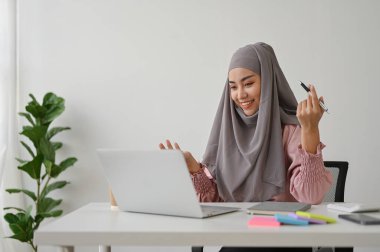 Genç Asyalı Müslüman iş kadını ekibiyle video konferansı yapıyor, ofis odasında oturuyor.. 