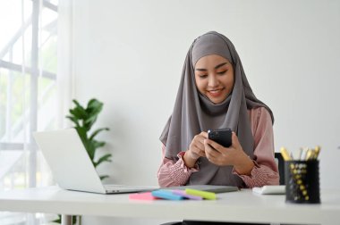Ofis odasında çalışan güzel bir Müslüman iş kadını, elinde akıllı telefon tutuyor. 