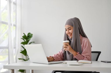 Genç, çekici Müslüman iş kadını ofisinde dizüstü bilgisayarla çalışıyor. 