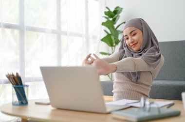 Genç, rahatlatıcı Müslüman kadın uzun saatler çalıştıktan sonra kollarını öne uzatıyor. ev kavramından çalışma