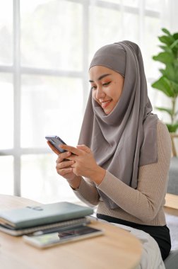 Genç, güzel Müslüman kadın oturma odasında otururken akıllı telefon kullanıyor. Boş zaman ve hobi konsepti