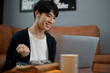 Genç ve sevimli Asyalı bir adam ailesiyle oturma odasında dizüstü bilgisayarında görüntülü konuşma yapıyor..