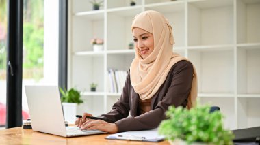 Güzel ve profesyonel bir Asyalı Müslüman iş kadını iş görevlerini bilgisayarında, ofisinde, masasında yapıyor..