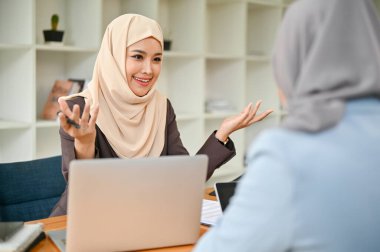 Kendine güvenen ve profesyonel Asyalı Müslüman bir iş kadını, fikirlerini paylaşıyor ve iş arkadaşıyla ofiste görüşüyor..