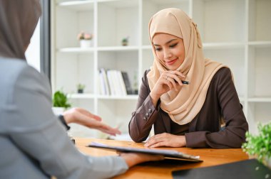 Güzel bir Asyalı Müslüman iş kadını mali danışmanıyla toplantıda, bir tablet ekrana bakarken birlikte bir yatırım planı hazırlıyor. kontrat, iş anlaşması