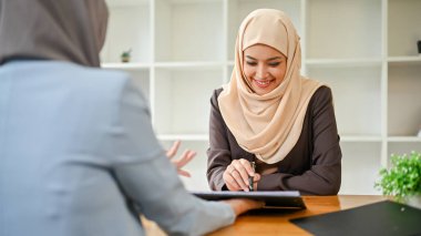 Güzel bir Asyalı Müslüman iş kadını mali danışmanıyla toplantıda, bir tablet ekranına bakarken birlikte bir yatırım planı hazırlıyor..