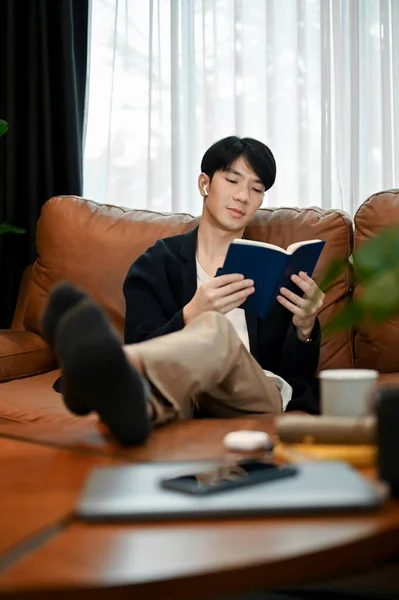 週末にはソファで読書をしている若いアジア人男性がいる 趣味の概念 — ストック写真