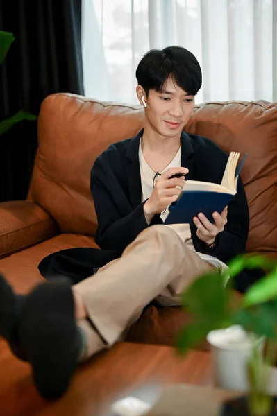 放松一下年轻的亚洲人 坐在沙发上看书和记笔记 给自己的工作时间 — 图库照片