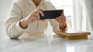Çok az kahve içilen bir kafede akıllı telefonunu kullanan rahat kazaklı bir kadının yakın plan görüntüsü. Video izlemek, mobil oyunlar oynamak.