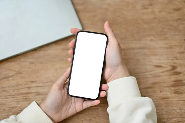 木製のテーブルの上にスマートフォンの白い画面のモックアップを保持している女性のトップビュー チャットメッセージモバイルアプリケーション — ストック写真