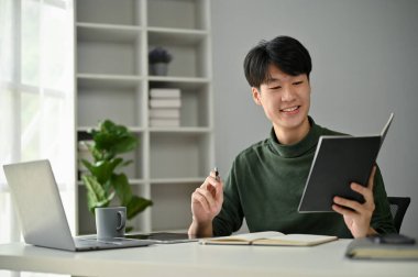 Gündelik giysiler içinde mutlu bir Asyalı adam masasında çalışırken randevu çizelgesini kontrol eder..