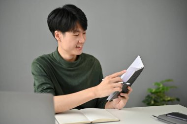 Yakışıklı ve güler yüzlü Asyalı bir adam çalışma saatlerini ve randevularını masasında çalışırken kontrol ediyor..