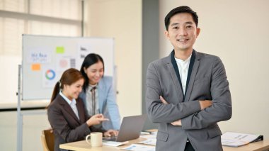 Milenyum Asyalı özgüvenli ve başarılı bir iş adamı veya resmi takım elbiseli bir erkek CEO toplantı odasında kollarını kavuşturmuş duruyor..