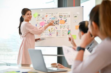 Kendine güvenen ve çekici bir Asyalı bayan teknoloji geliştirici ekibiyle birlikte yeni bir projeyi tartışarak ve beyin fırtınası yaparak toplantıya öncülük etti..