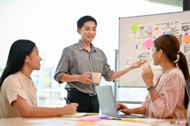 Profesyonel bir Asyalı erkek teknisyen projesini toplantıda meslektaşlarına sunuyor. Danışmanlık, beyin fırtınası, birlikte çalışma, takım çalışması.