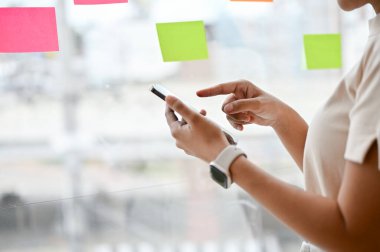 Ofisinin penceresinde dikilirken akıllı telefonunu kullanan bir kadının yakın plan görüntüsü. metin, sohbet, mesaj, sosyal medya, mobil uygulama