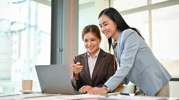 A beautiful millennial Asian female boss is helping her employee on a project, discussing and sharing her ideas on the project, and working together in the meeting room.