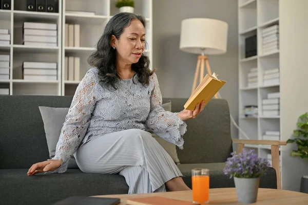一个快乐 退休的亚洲女人喜欢周末在客厅的沙发上看书 生活方式概念 — 图库照片