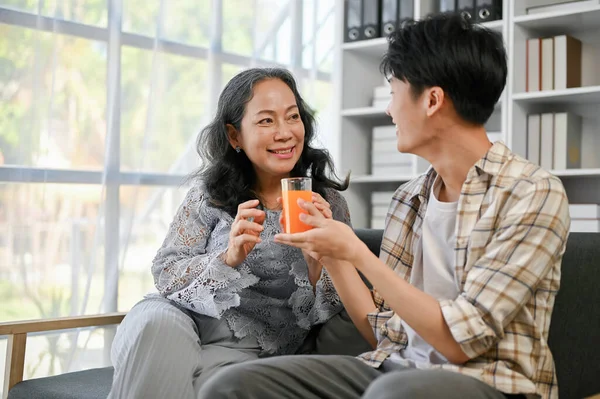 귀엽고 마음씨좋은 아시아인 손자가 할머니에게 오렌지 주스를 잔드리면서 집에서 시간을 — 스톡 사진