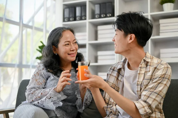 귀엽고 관심이 아시아인 손자가 할머니에게 오렌지 주스를 잔주면서 집에서 시간을 — 스톡 사진