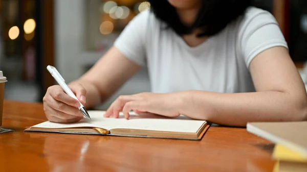 カフェでリラックスしながら本や日記に何かを書いている若いアジアの女性のクローズアップイメージ — ストック写真