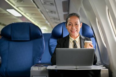 Gülümseyen ve başarılı bir Asyalı iş kadınının portresi iş seyahatinde, koltuğunda taşınabilir laptopuyla oturuyor..