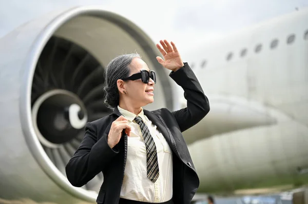 stock image A successful and confident mature Asian businesswoman in sunglasses and a formal business suit boards a plane for her business trip. Businesspeople and transportation concept