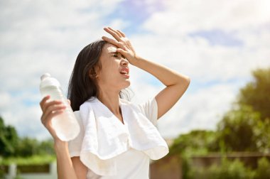 Spor giyimli yorgun ve terli bir Asyalı kadın güneşli bir yaz gününde parkta koşarken sıcak hava dalgalarıyla savaşıyor. Yaz etkinliği, sıcak çarpması, susuzluk.