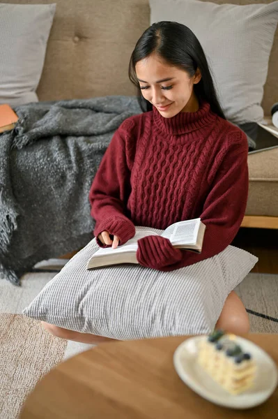 冬日里 一个穿着舒适毛衣的美丽的亚洲女人的画像喜欢在客厅里看书 — 图库照片