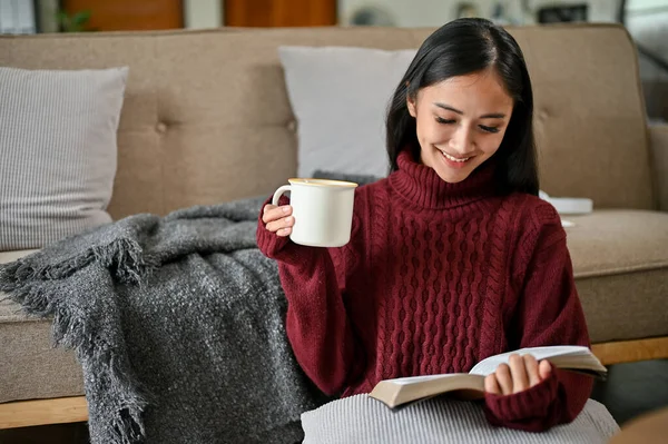 一位穿着舒适毛衣的迷人而轻松的亚洲女人喜欢在冬日里在客厅看书 喝热咖啡 休闲和业余爱好概念 — 图库照片